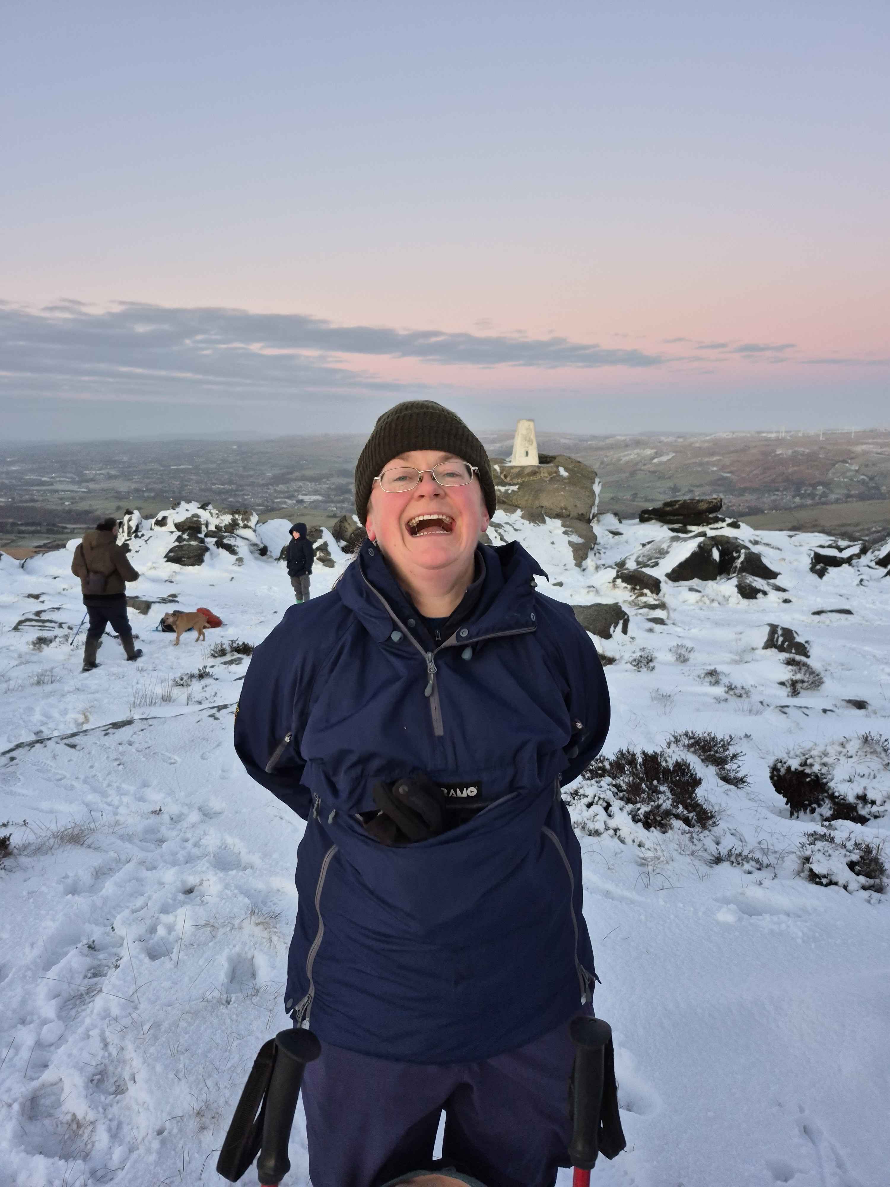 Liz standing on snowy hillside with trig point